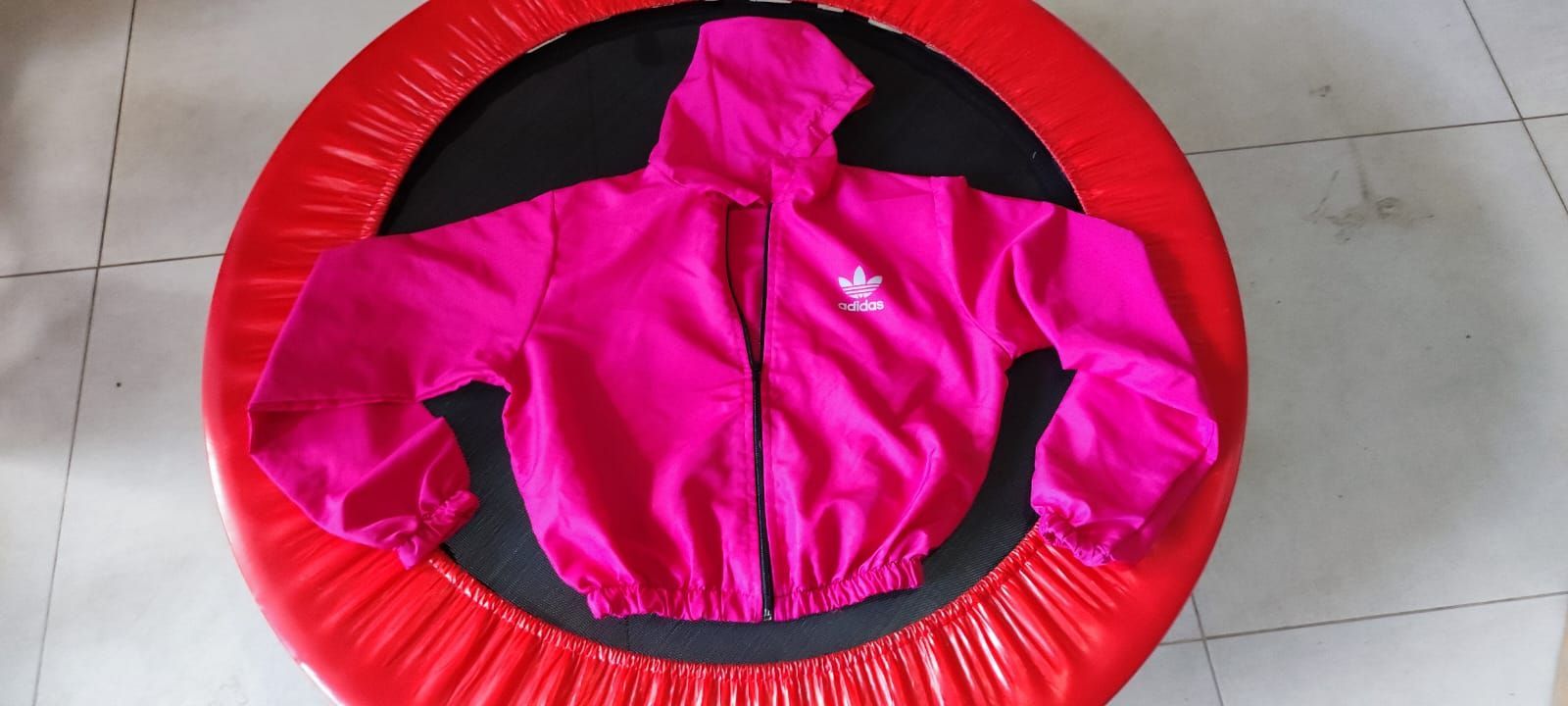 Chaqueta con capucha rosa de Adidas sobre una cama elástica roja.