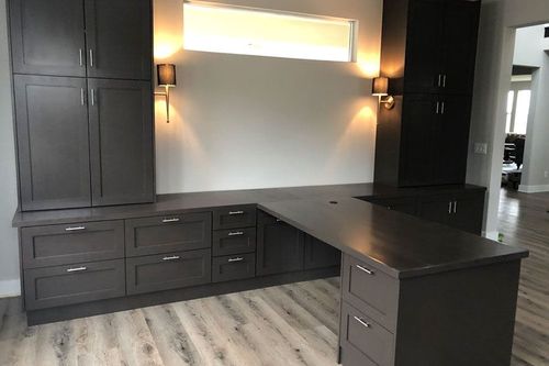 Dark built-in desk with cabinets and drawers in a home office nook, under wall sconces and a window