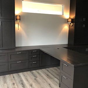 Modern dark wood home office with built-in cabinets, black desk, wall sconces, and frosted window.