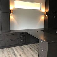 Modern dark wood home office with built-in cabinets, black desk, wall sconces, and frosted window.