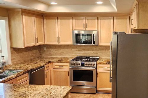 Modern kitchen with light wood cabinets, granite counters, stainless steel appliances, and mosaic tile backsplash