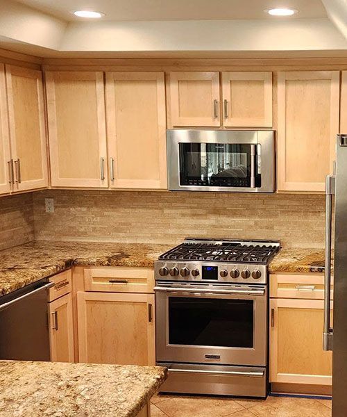 Modern kitchen with light wood cabinets, stainless steel stove and microwave, and granite countertops.