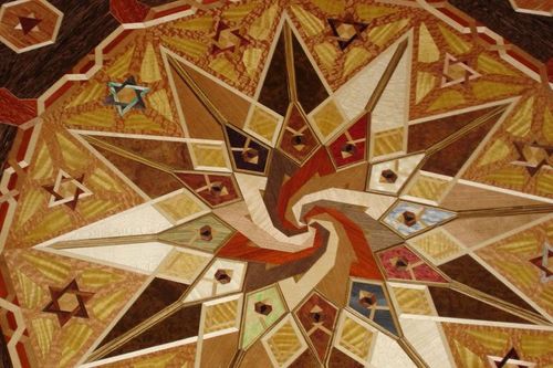 Abstract geometric mosaic with a central spiral, starburst patterns, and warm red, gold, and cream tones