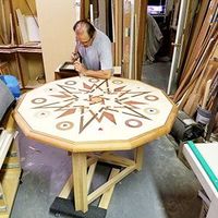 Person working on an octagonal wooden table with decorative inlays in a workshop.