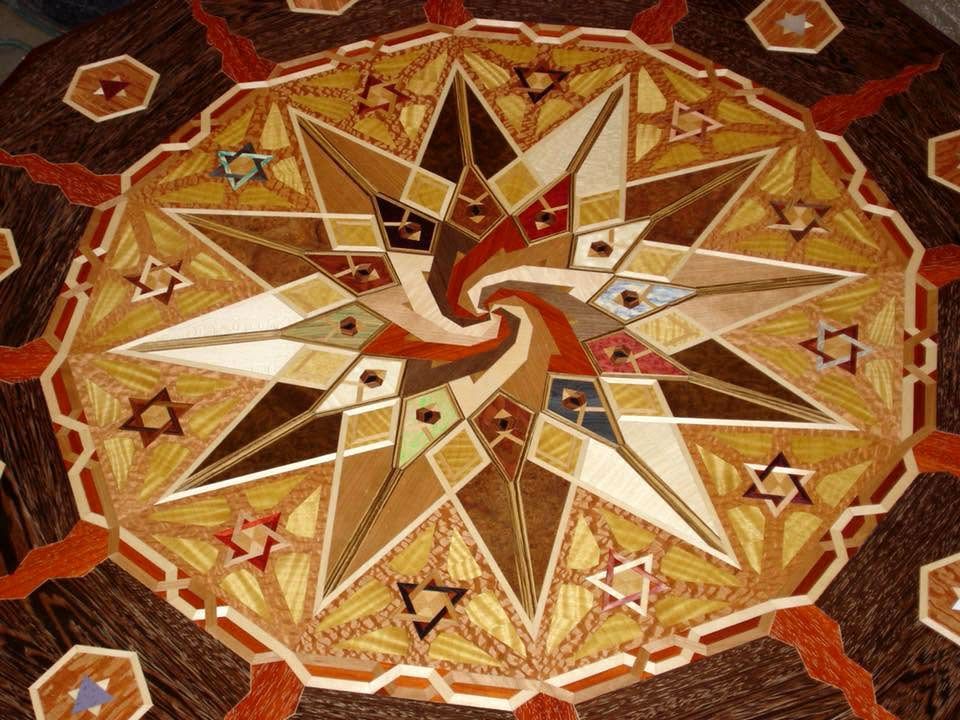 Geometric mosaic compass rose in gold, brown, and white with a red center on a patterned floor.
