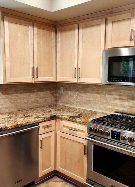 Compact kitchen corner with light wood cabinets, granite counters, stainless dishwasher, and gas range and microwave.