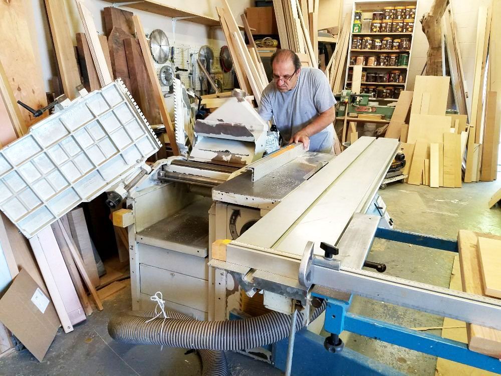 Man in a woodworking shop using a table saw among lumber and tools