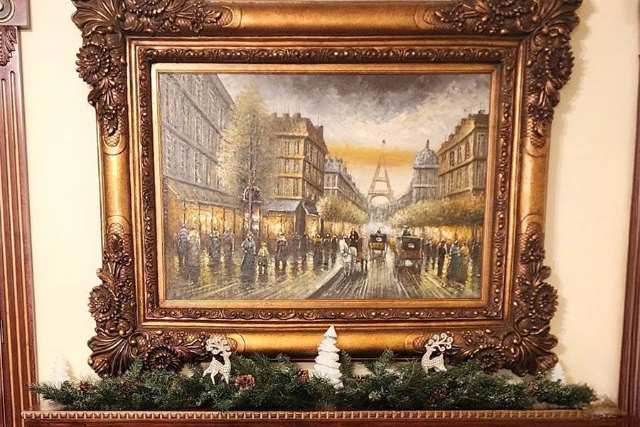 Framed painting of a rainy Paris street scene above a mantel with holiday greenery and small figurines
