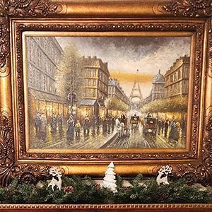 Framed painting of a rainy Paris street with the Eiffel Tower in the distance, above a holiday garland with figurines