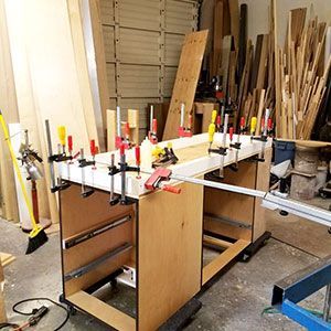 Woodworking bench with many clamps securing boards in a cluttered workshop