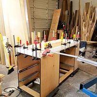 Woodworking bench with many clamps securing boards in a cluttered workshop