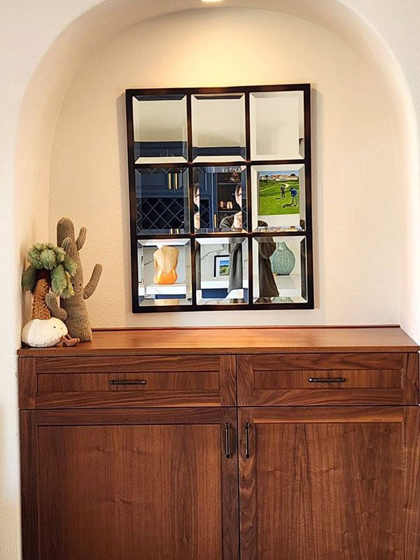 Wooden cabinet in an arched alcove with a decorative mirror and small cactus display