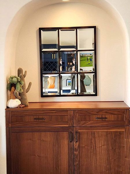 Wooden cabinet in an arched alcove with a decorative mirror and small cactus display
