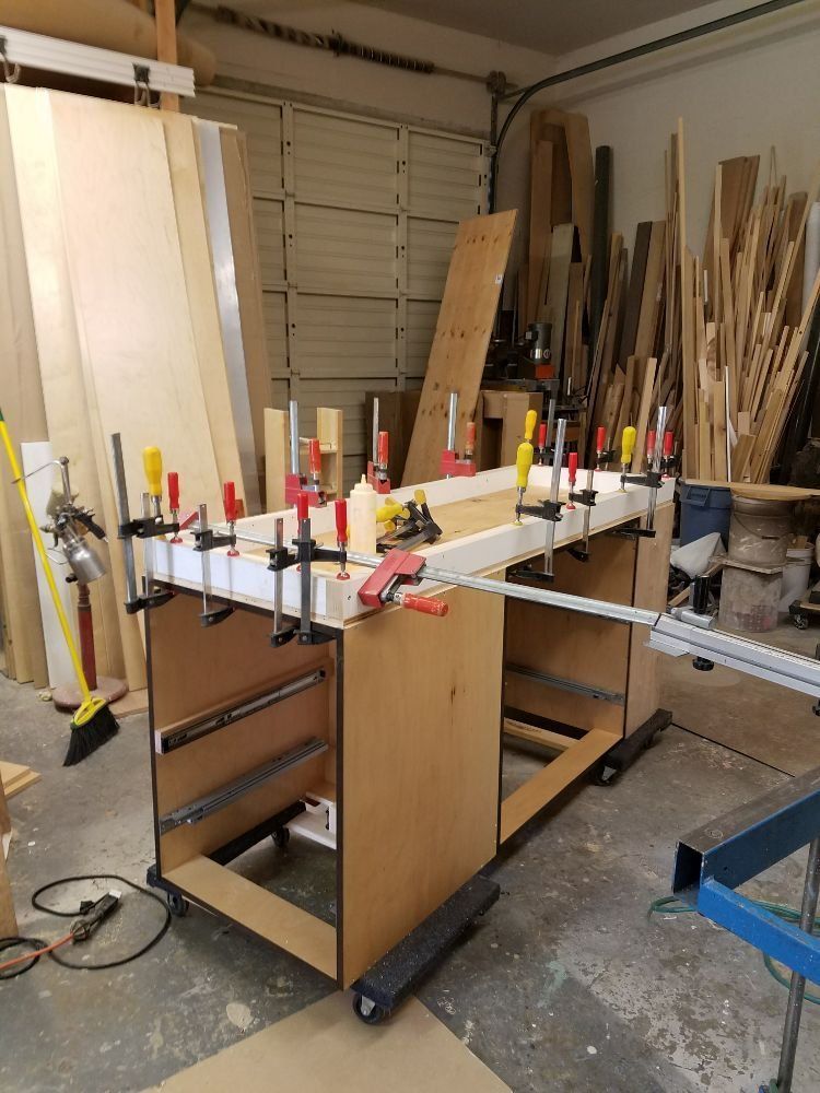 Woodworking shop with a clamp-filled workbench, lumber stacks, and tools in a garage-like space