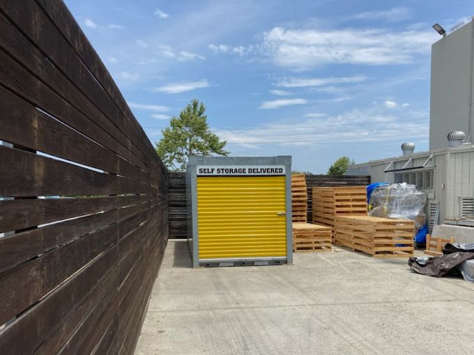 A yellow storage container is sitting next to a wooden fence.