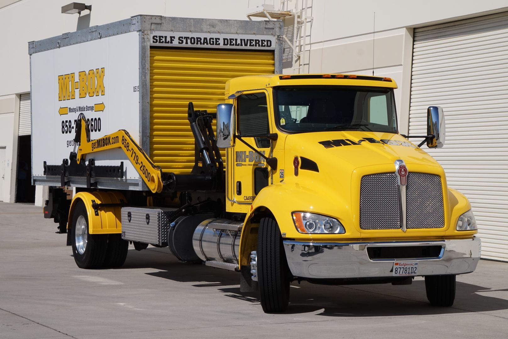 A yellow truck is parked next to a white box that says self storage delivery
