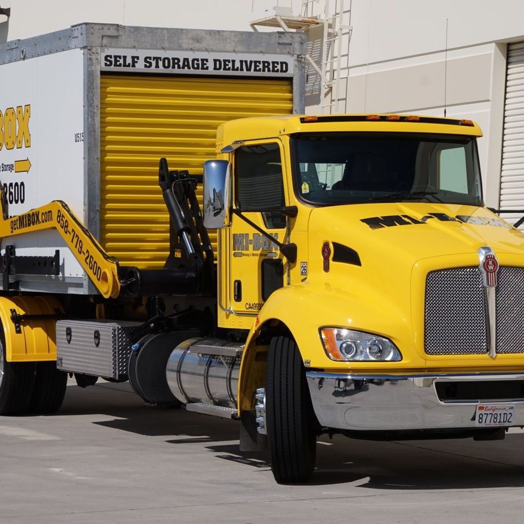 A yellow truck is parked next to a white portable storage container that says self storage delivered