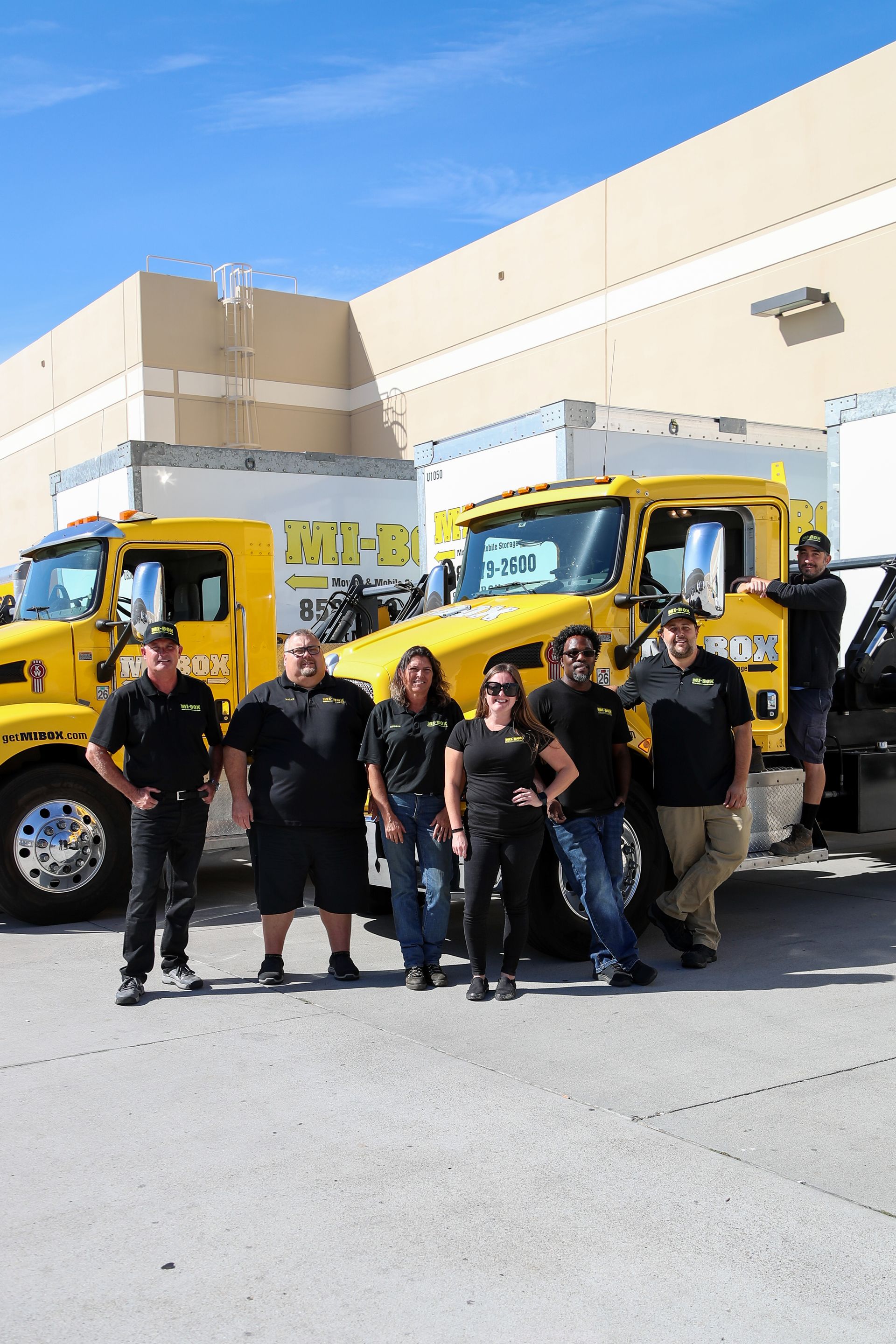 A group of people are posing for a picture in front of yellow trucks.
