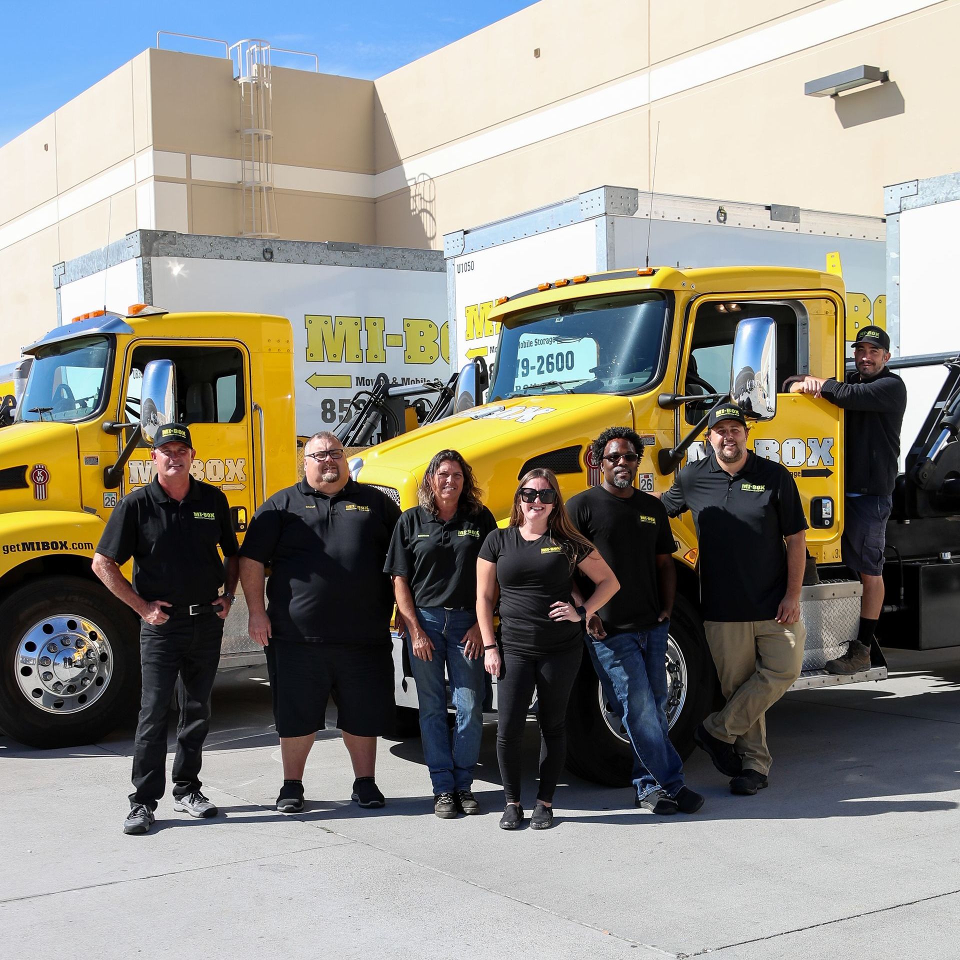 A group of people posing for a picture in front of a yellow truck that says m-b