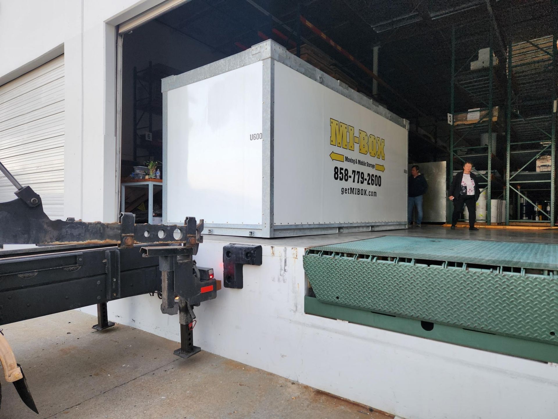 Large white machine being loaded onto a truck with a forklift inside a warehouse.