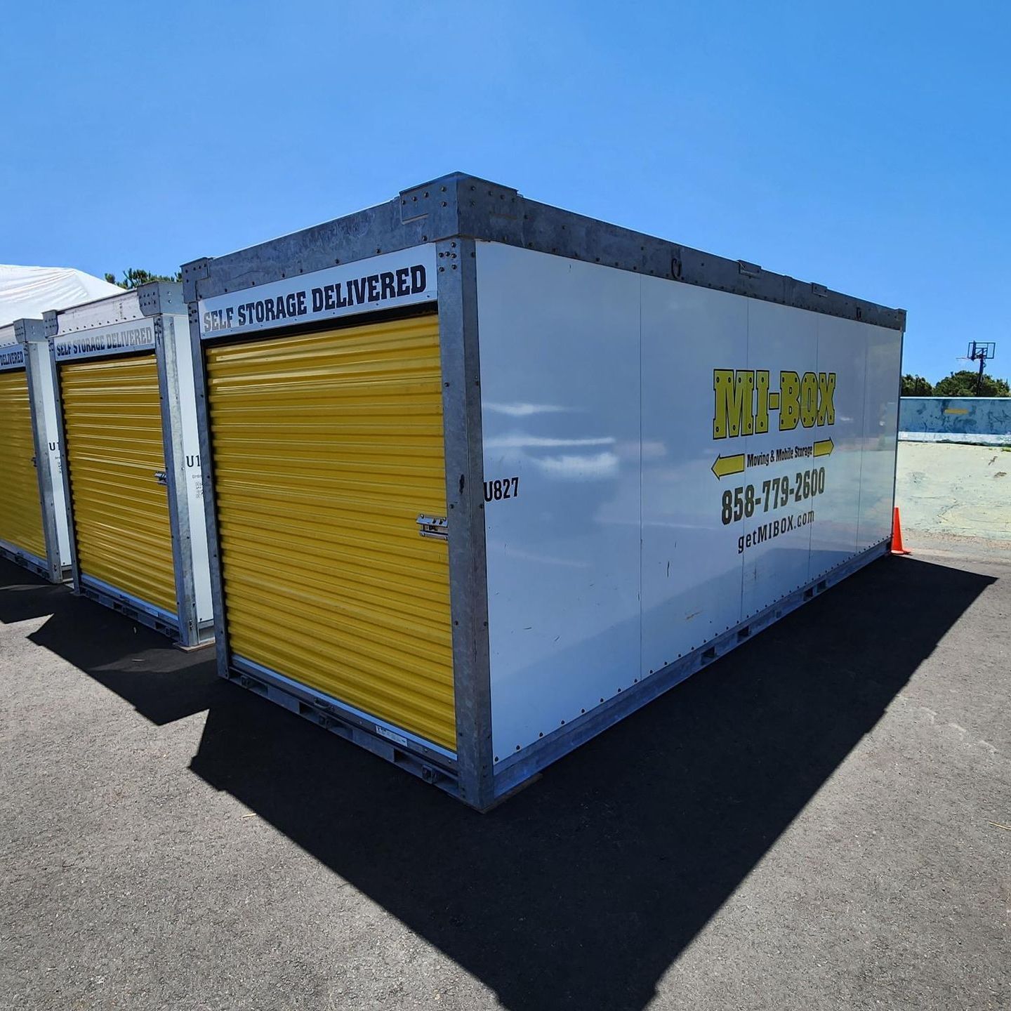 A white container with yellow shutters is parked in a parking lot.