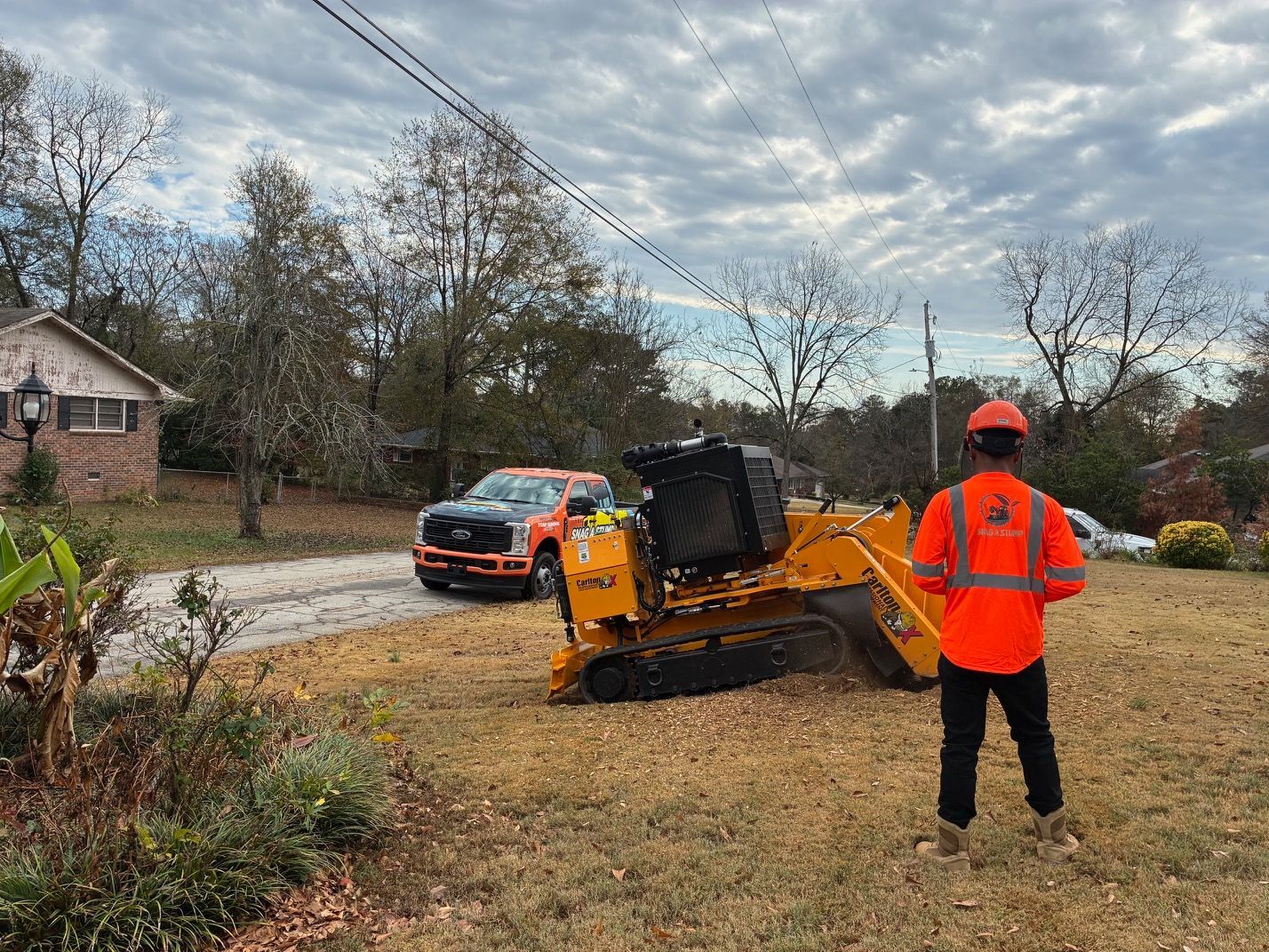 Person using chainsaw to cut through a fallen tree trunk in a grassy outdoor setting.