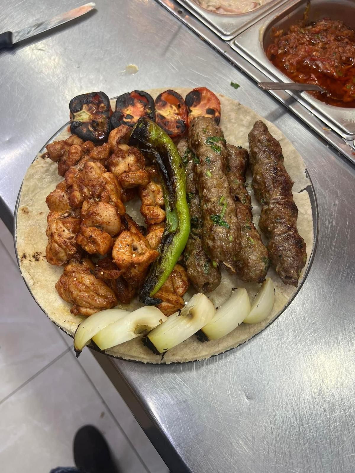 בשר וירקות צלויים על לחם שטוח במגש מתכת עם רוטב אדום בצד