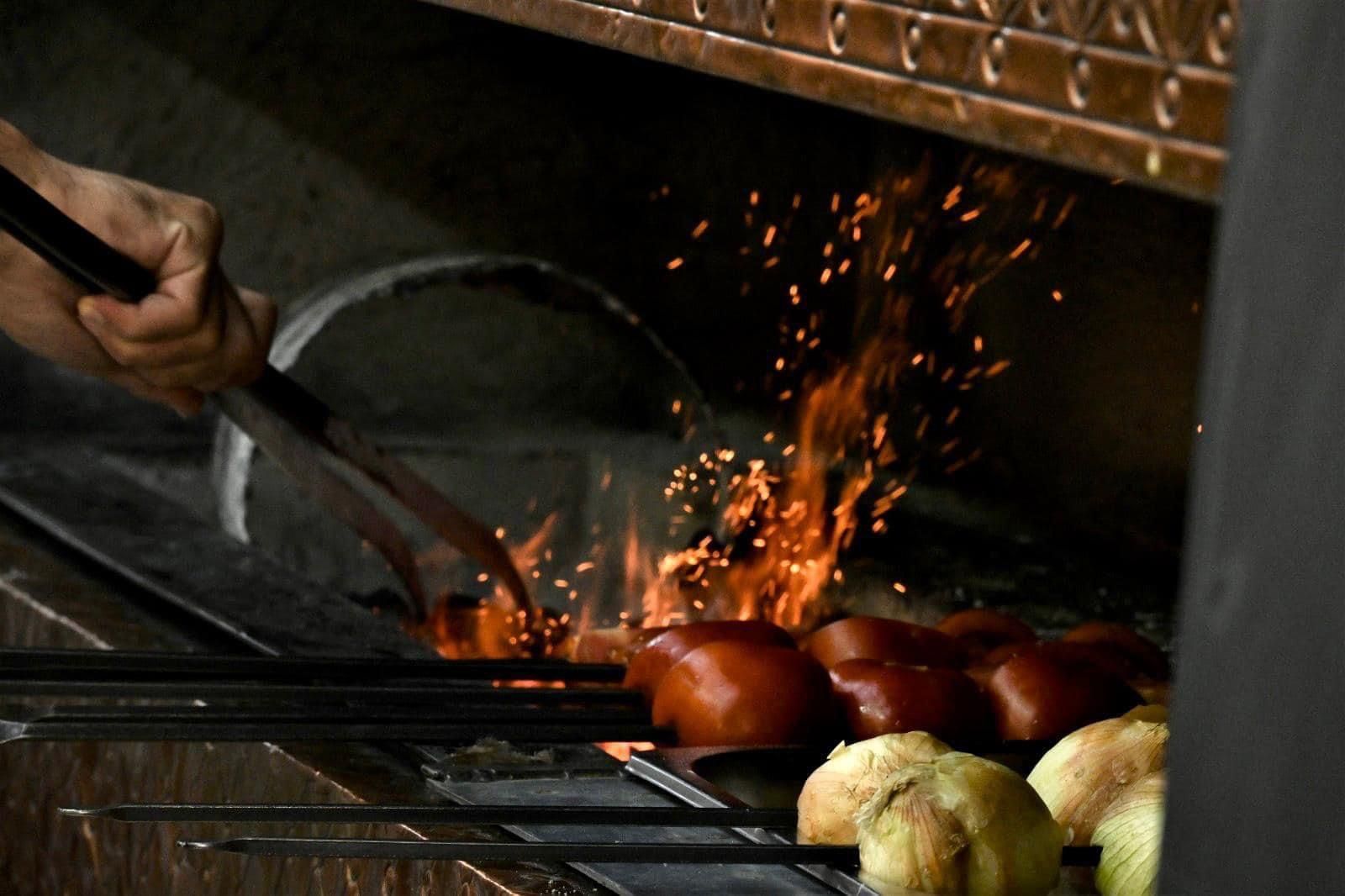 ירקות צלויים על להבה גלויה כשניצוצות עפים בזמן שיד מדליקה אותם על מנגל.