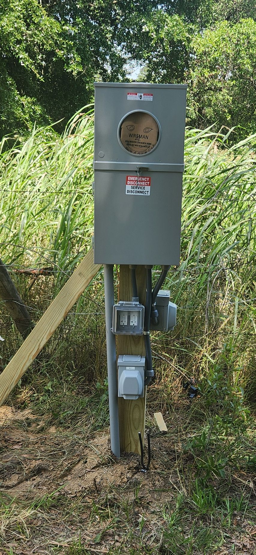 Gray electrical meter box mounted on a wooden pole with foliage in the background.