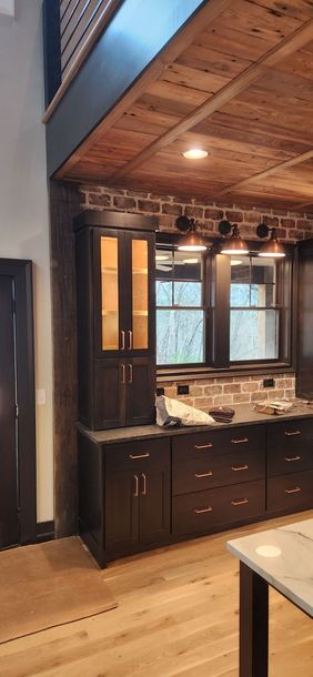 Interior view of a kitchen with dark cabinetry, brick accent wall, and wooden ceiling.