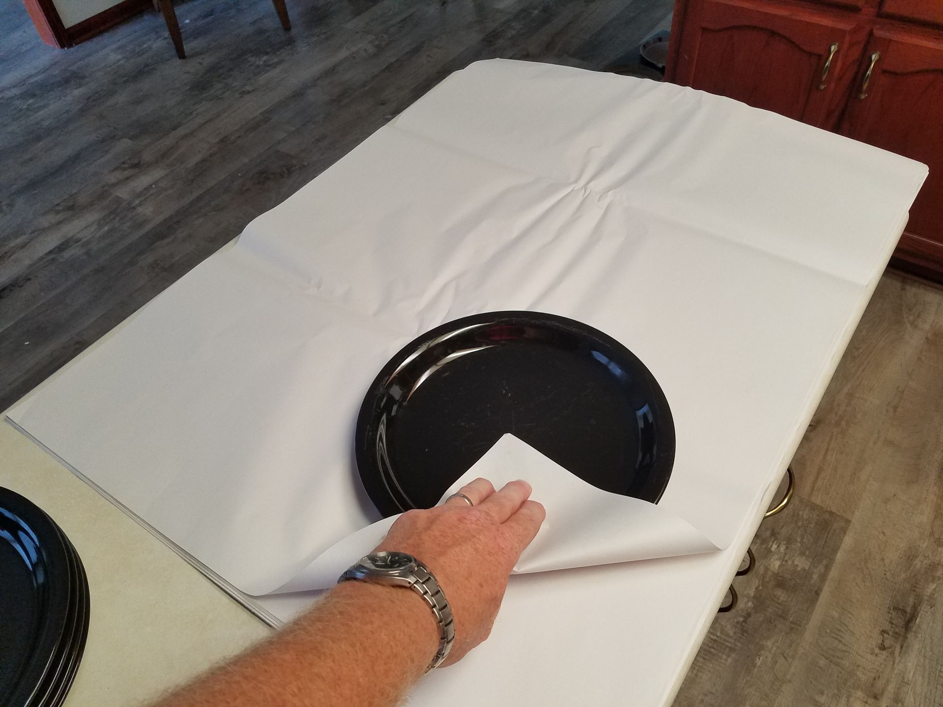 a person wearing a watch holds a black plate on a white cloth
