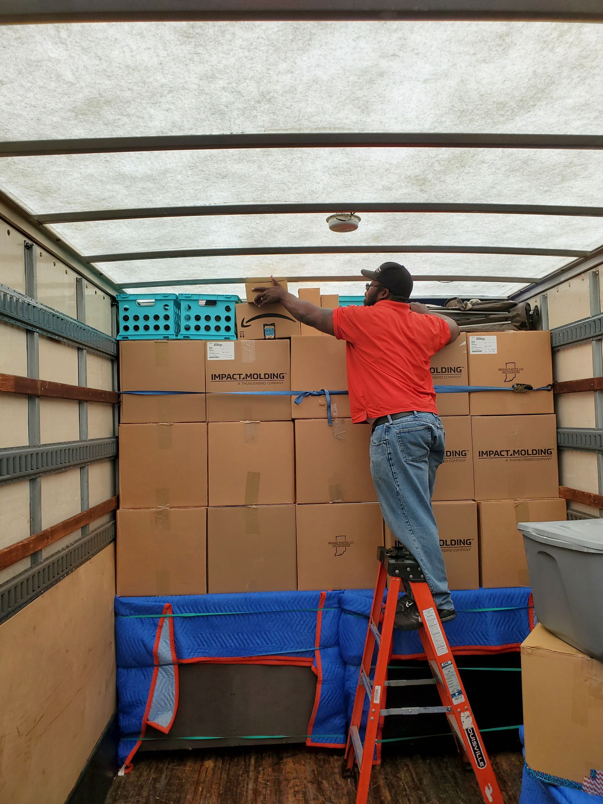 a man standing on a ladder in front of a truck full of boxes that say impact molding