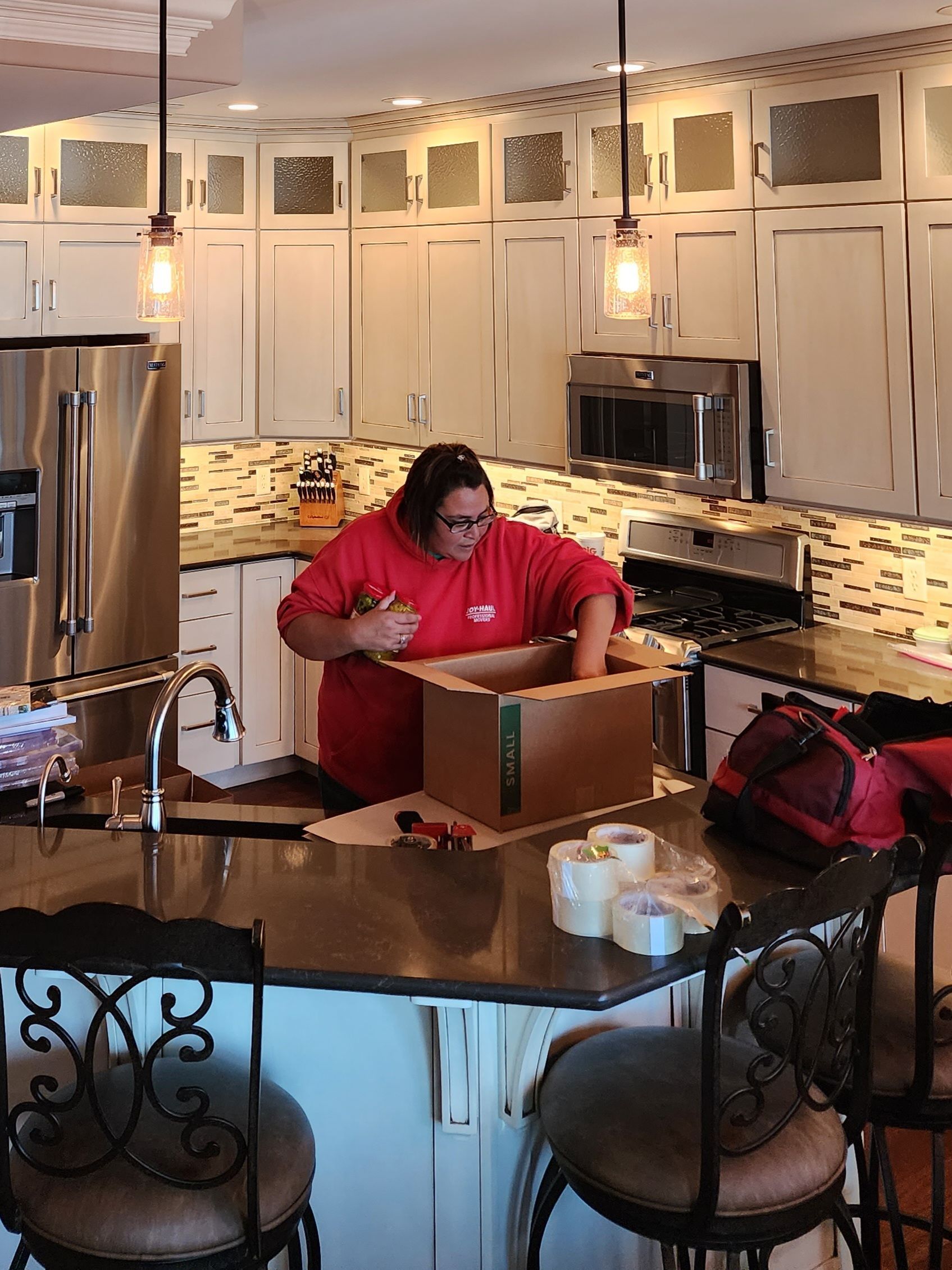 a woman in a red sweatshirt is packing a cardboard box with a label that says