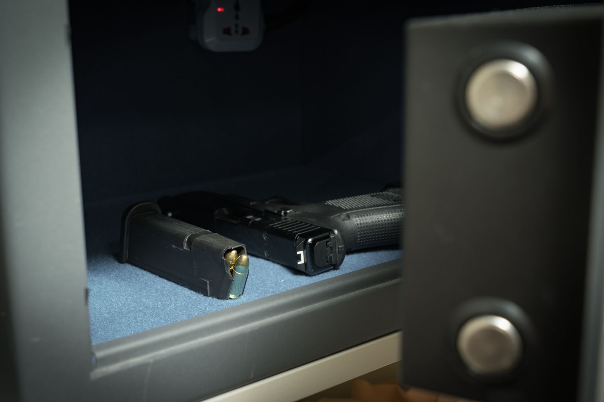 Open gun safe with a handgun and magazine. Black metal safe, blue interior, partially open door.