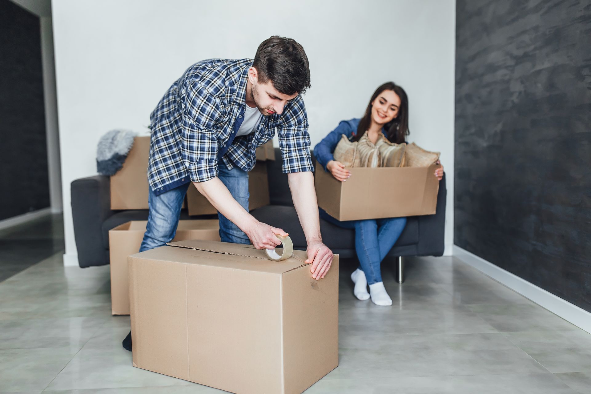 Man taping a cardboard box, woman holding a box, moving.