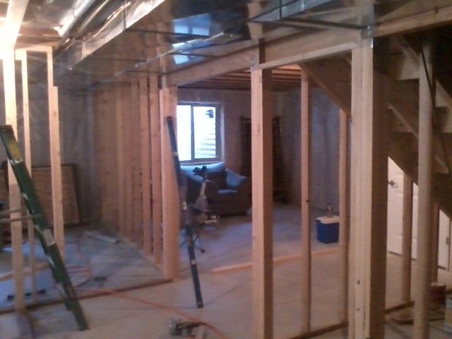 Unfinished basement with wooden framing, revealing a room, stairs, and a window.