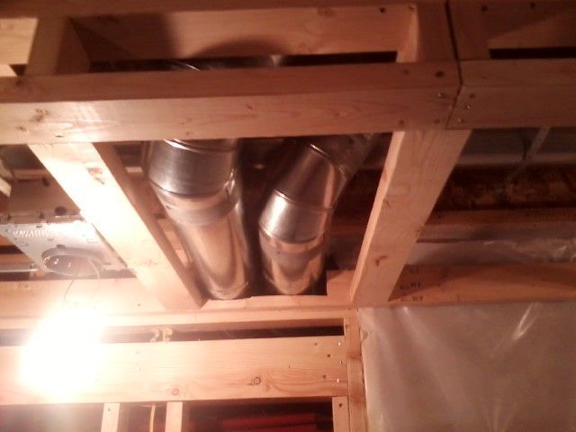 Two silver ducts angled in a wooden framework, likely ceiling construction, in a room.