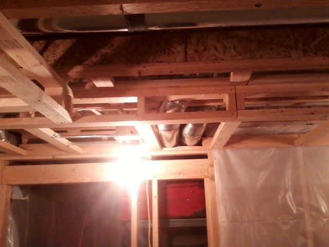 Wooden beams and ductwork in a partially finished basement. Bright light source illuminates the scene.
