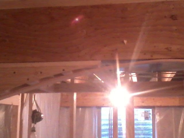 Wooden ceiling and beams under construction, with bright light source shining through.