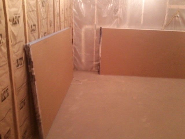 Interior corner of a room, drywall boards leaning against insulation. Brown and tan colors.