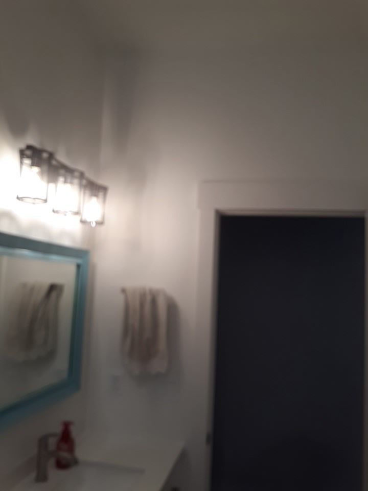 Bathroom with blue-framed mirror, vanity, and lit light fixture above. A towel hangs on a rod. A dark blue door is on the right.