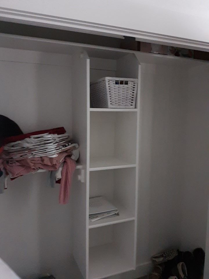 White closet with built-in shelves. A basket sits on the top shelf, clothes on a rod to the left.