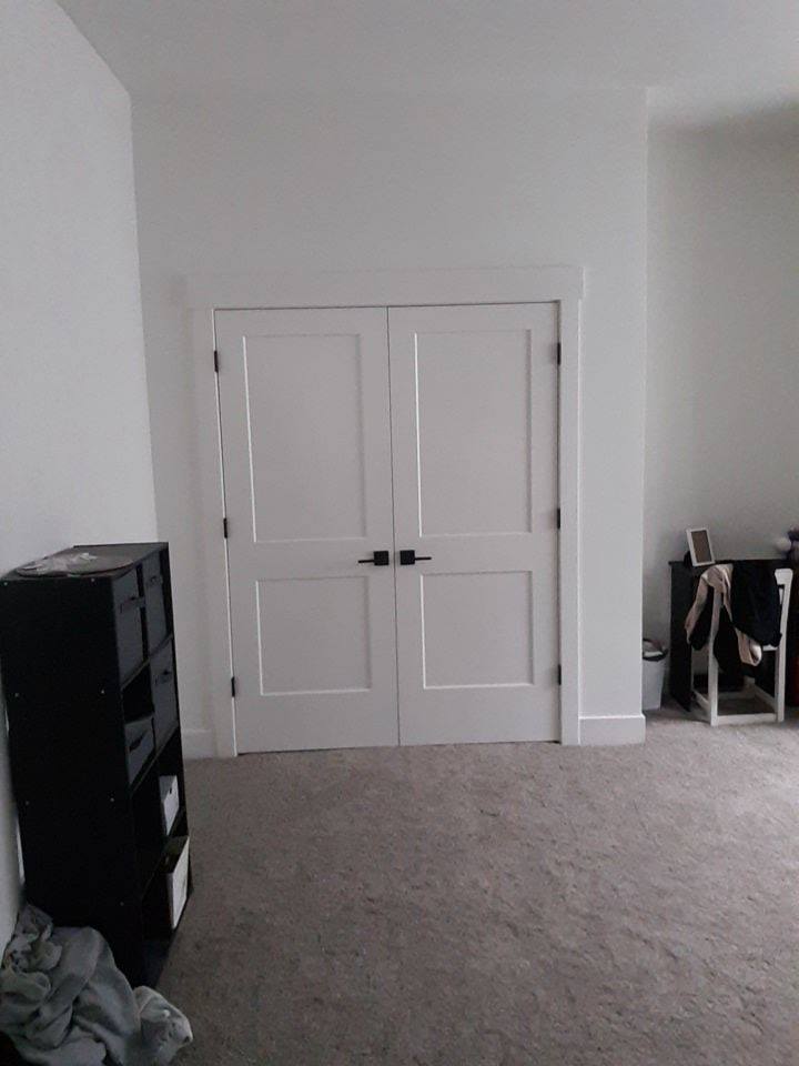 White double doors in a room, with a black shelving unit on the left and a desk to the right, gray carpet.