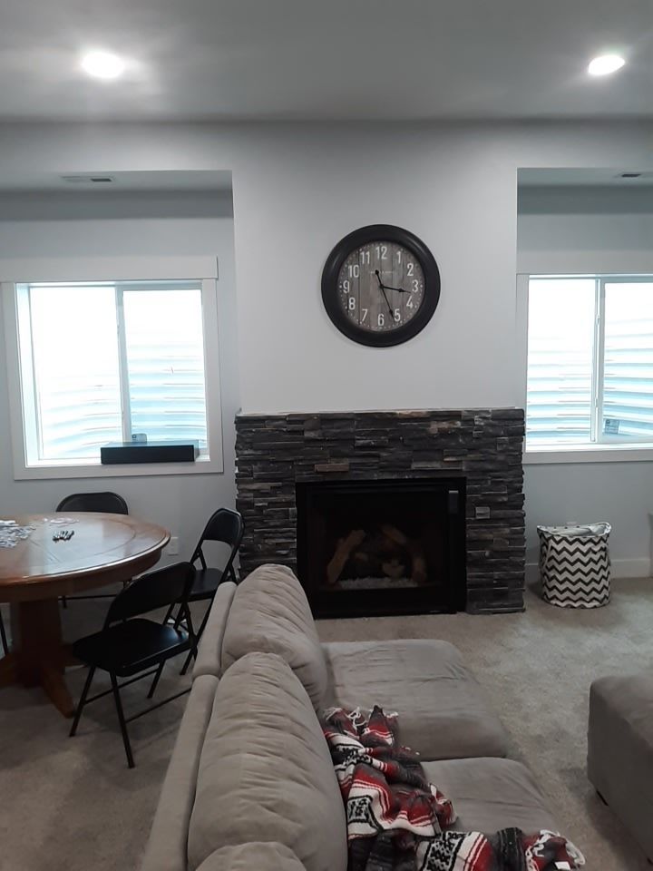 Living room with fireplace, clock, windows, sofa, table, chairs, and basket.