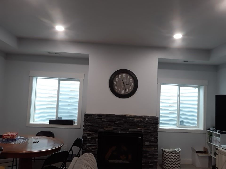 Living room with fireplace, windows, clock, and dining table. Stone fireplace with a circular clock above.