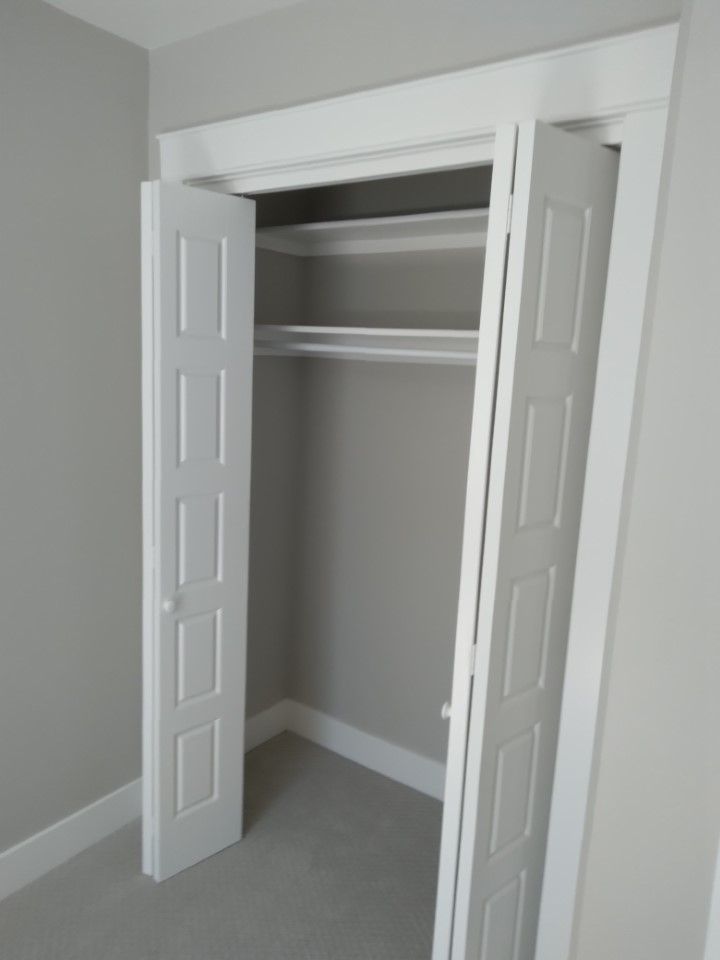White bi-fold closet doors open in a gray-walled room, revealing shelves and a clothes rod.
