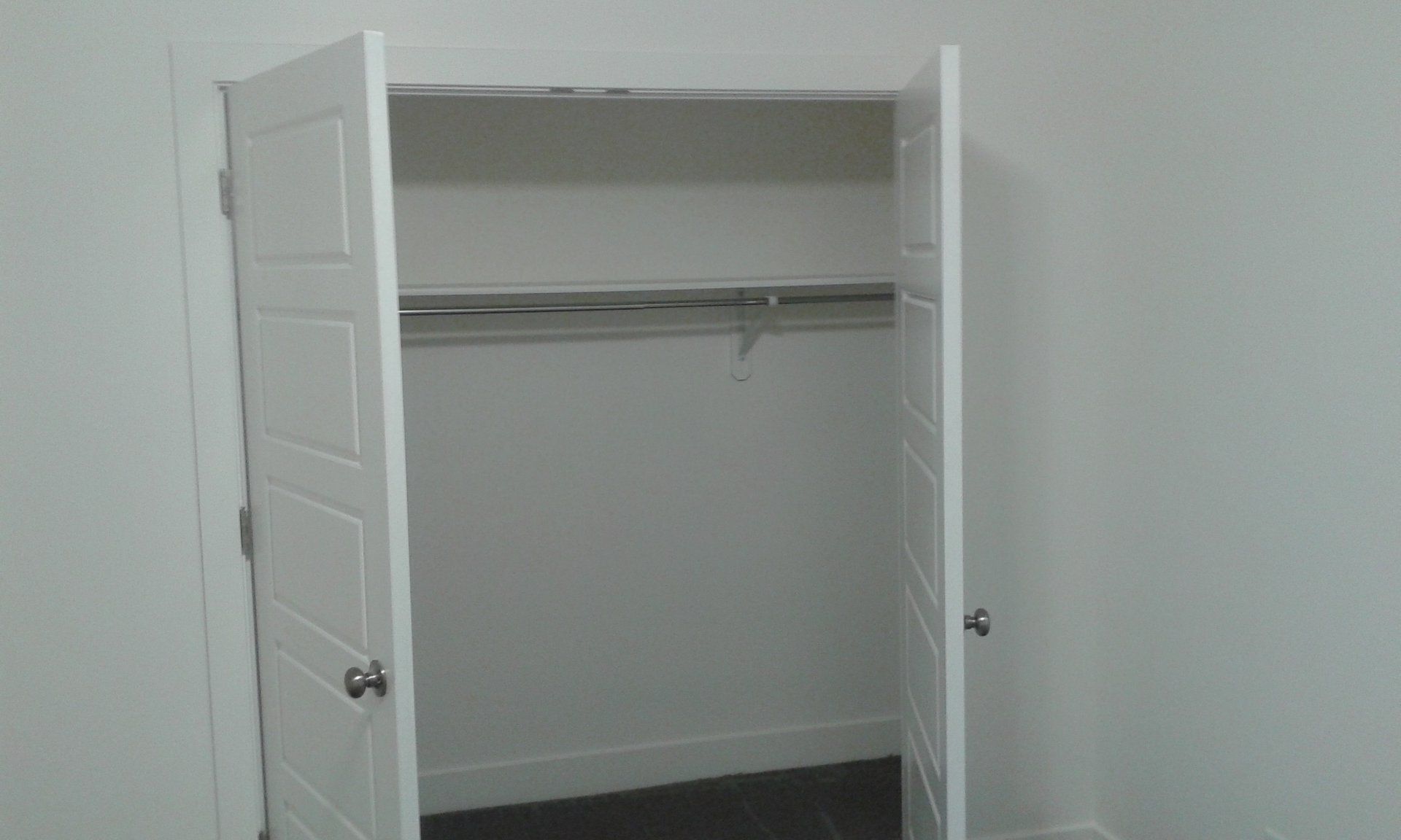 White closet with open doors, hanging rod, and shelf. Empty interior against white walls.