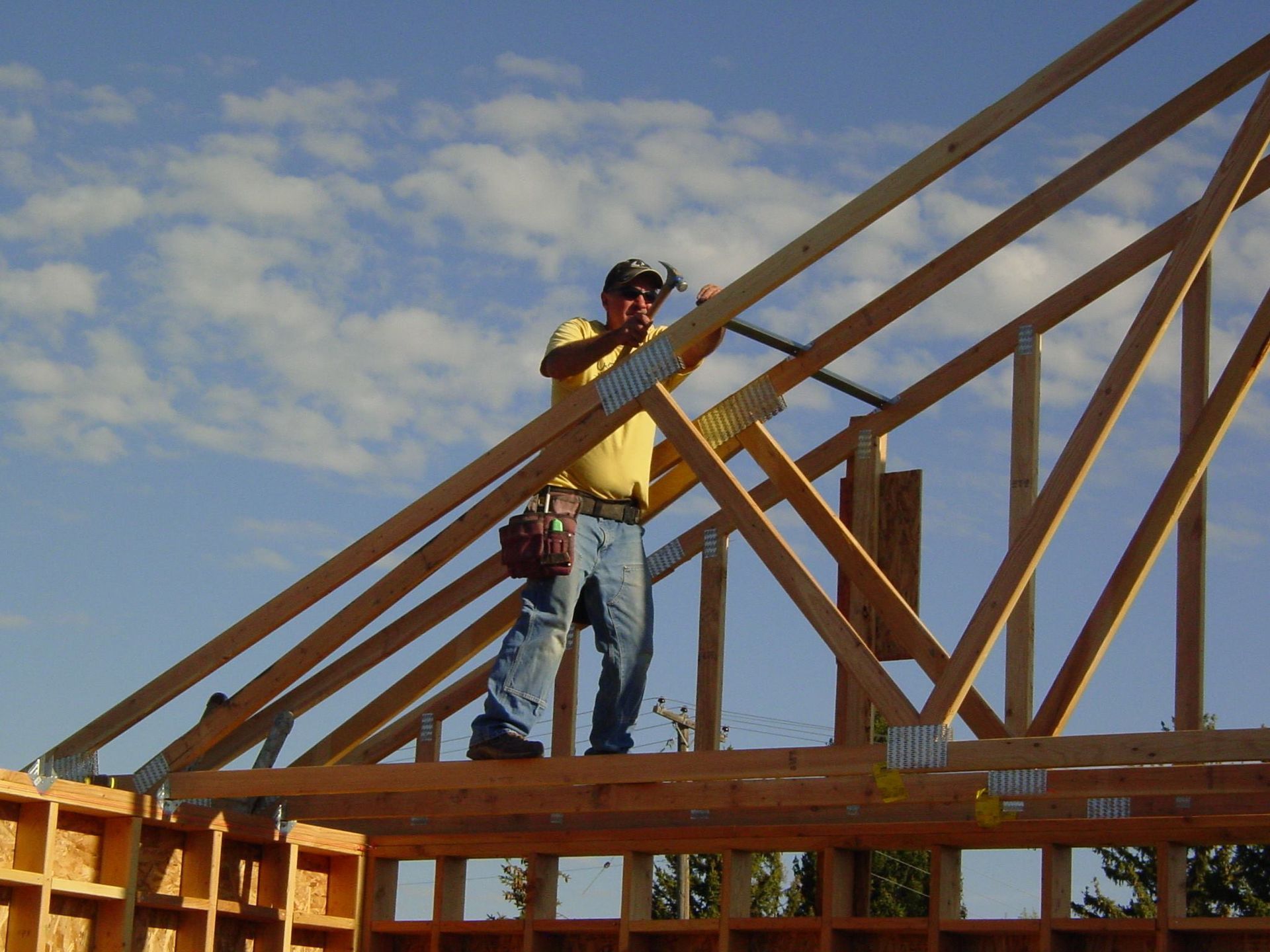 Construction worker hammering roof truss on a sunny day.