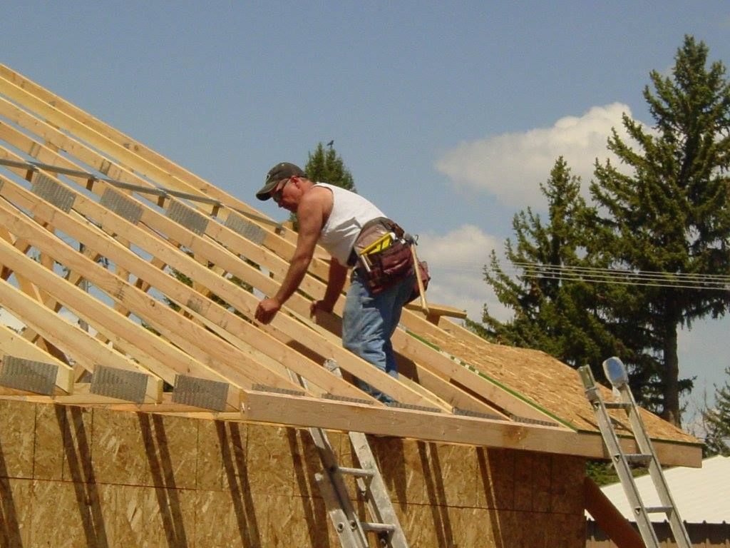 A construction worker on a roof wearing a tool belt, inspecting wooden beams. Sunny day.
