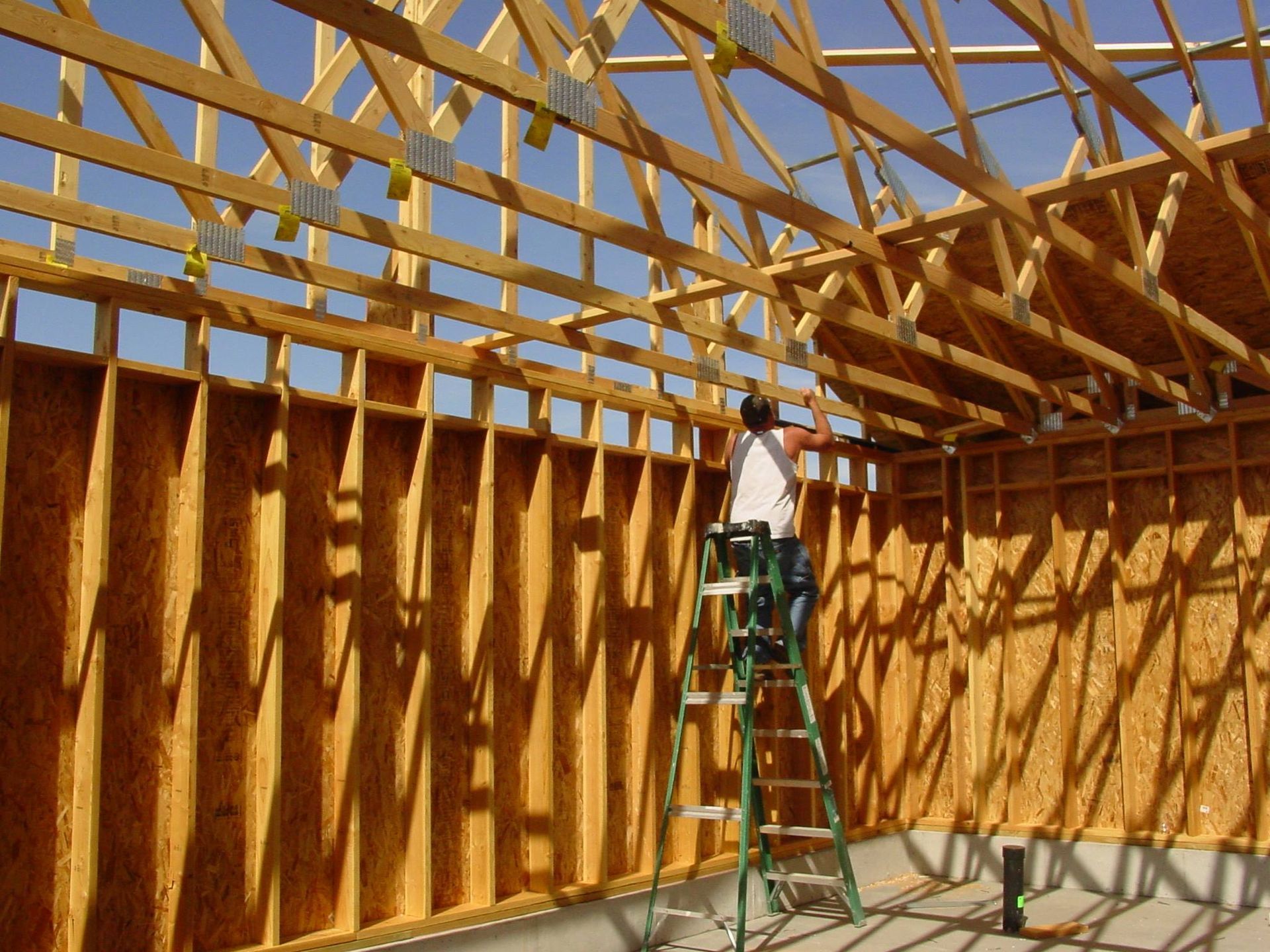 Construction worker on a ladder inside a wood-framed building under construction, installing ceiling beams.